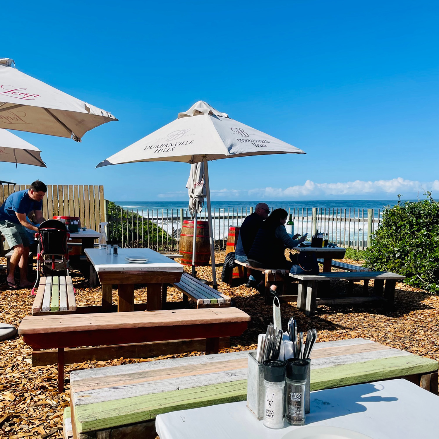 Het terras met picknicktafels van Enrico's restaurant met in de verte de oceaan